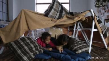 两个可爱的混合种族小女孩看有趣的视频在数码平板电脑上，<strong>因为</strong>他们躺在一起在小房间做
